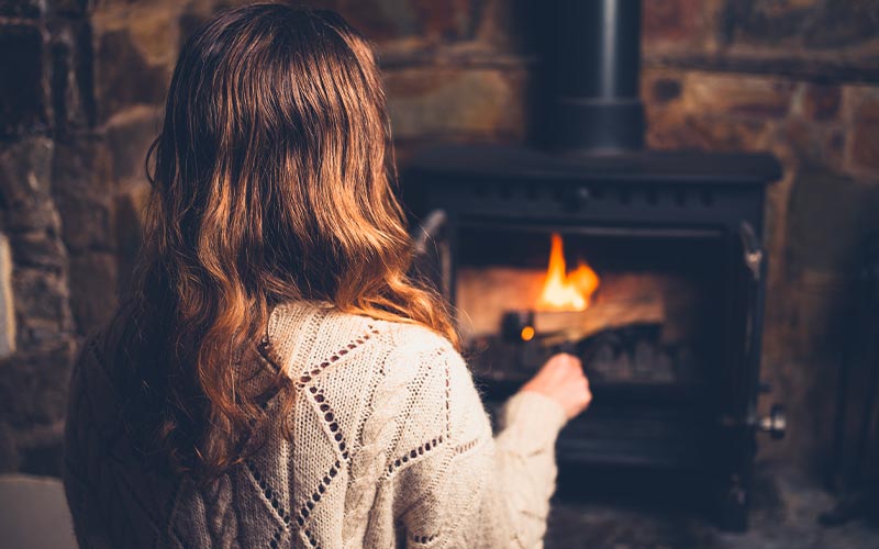 femme se réchauffant près d'un poêle à bois